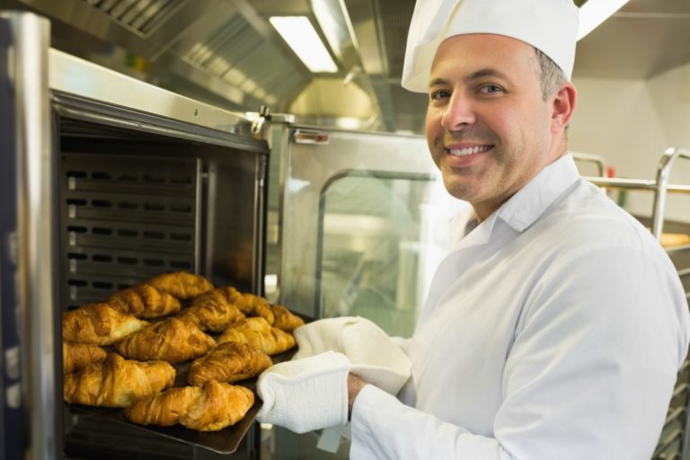 Baker bringing out croissants from the oven