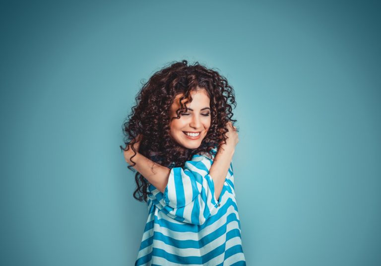 woman with curly hears wearing blue striped shirt hugging herself